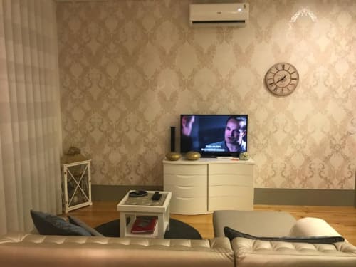 Sala de estar moderna em apartamento no Porto com sofá creme, TV de plasma, piso de madeira e papel de parede bege estampado