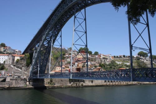 Histórica ponte de ferro sobre o Rio Douro no Porto com edifícios na encosta e arquitetura colorida