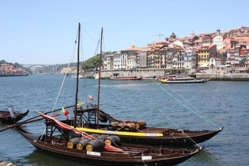 Barcos tradicionais de madeira no Rio Douro do Porto com edifícios históricos coloridos na encosta, Portugal