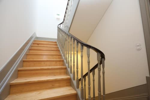 Escadaria de madeira com corrimão metálico em edifício residencial no Porto, levando aos andares superiores com paredes creme