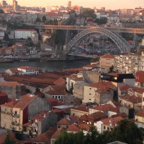 Paisagem urbana do Porto ao pôr do sol com a icônica ponte em arco sobre o rio Douro e edifícios tradicionais com telhados em terracota