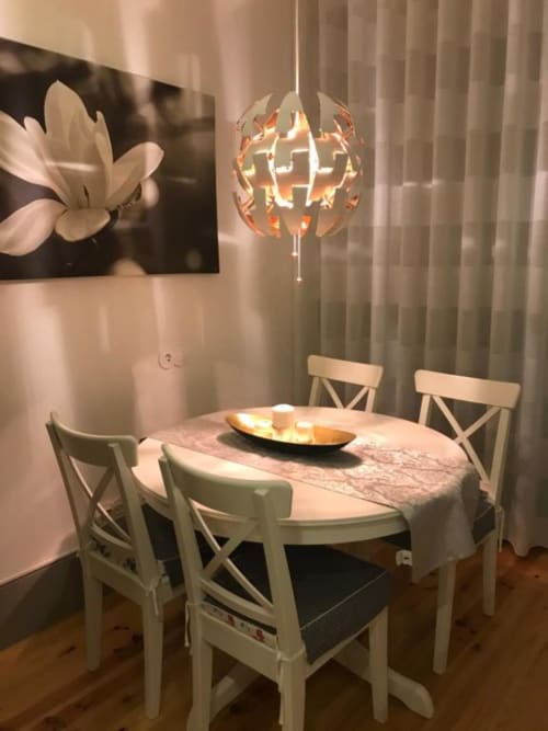Elegante sala de jantar em apartamento no Porto com mesa redonda, cadeiras brancas e luminária decorativa suspensa sobre a mesa