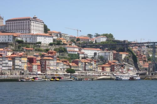 Vista panorâmica da margem do Porto com edifícios coloridos, barcos e ponte do Rio Douro