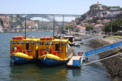 Barcos turísticos amarelos atracados no Porto com a Ponte Dom Luís e edifícios coloridos na encosta ao fundo