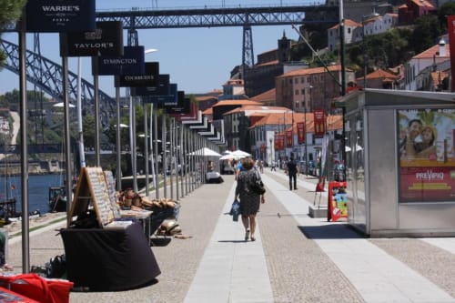 Passeio ribeirinho no Porto com tabuletas de caves de vinho, pedestres e arquitetura histórica sob céu azul