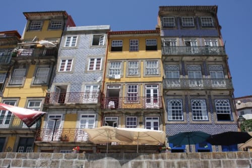 Edifícios históricos coloridos no Porto, Portugal com fachadas amarelas, azuis e azulejos sob céu claro