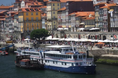 Edifícios coloridos à beira-rio e barco turístico no histórico Ribeira do Porto com terraços cheios de gente