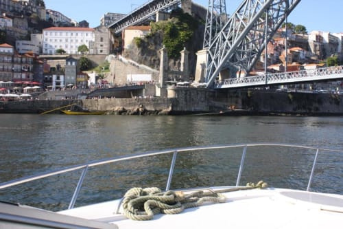 Corrimão do convés do barco com vista sobre o Douro do Porto, ponte de ferro e edifícios históricos à beira-água