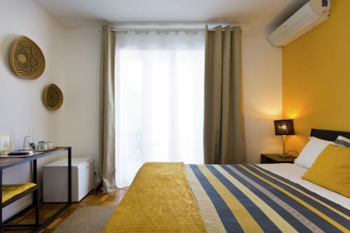Bright bedroom with yellow accent wall, striped bedding, desk, and city views at 100 Contos B&B Porto