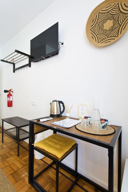 Modern workspace at 100 Contos Porto B&B with wooden desk, black frame furniture, yellow cushioned stool, electric kettle,
