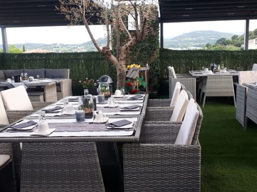 Élégante terrasse de restaurant en plein air à Luberon L'Hôtel à Apt avec mobilier en rotin, vue sur les montagnes et haie verdoyante.