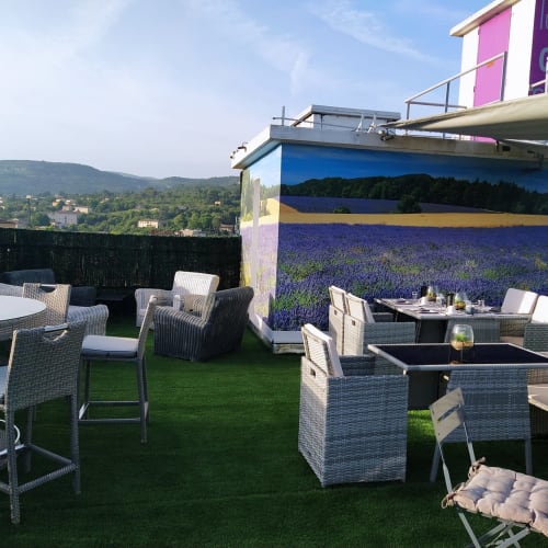 Terrasse sur le toit de Luberon L'Hôtel à Apt, France : mobilier en rotin, fresque de champs de lavande et vue sur la vallée.