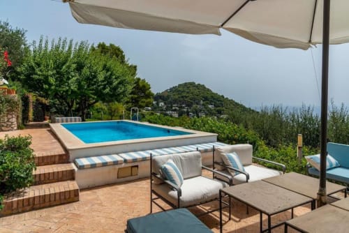 Terrazza piscina di lusso a La Conciergerie Capri con lettini, ombrelloni e vista sulle colline