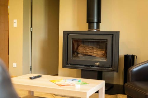 Poêle à bois contemporain dans le salon douillet du gîte Accolade, aux murs crème et sièges en cuir
