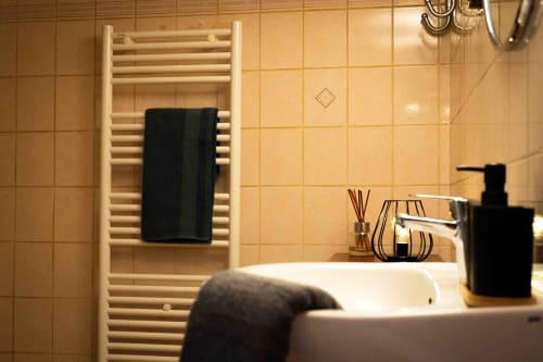 Salle de bain moderne avec porte-serviettes chauffant et serviette noire, carrelage beige, lavabo équipé au gîte Accolade
