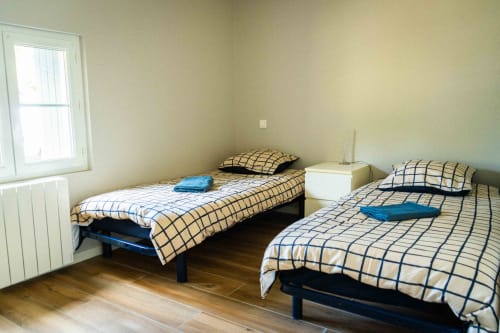 Deux lits simples aux draps à carreaux dans une chambre lumineuse du gîte Accolade Châteaudun, avec parquet et grandes