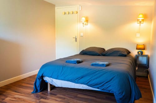 Chambre accueillante du gîte Accolade à Châteaudun avec literie bleue, parquet, lampe de chevet et porte de salle de bain