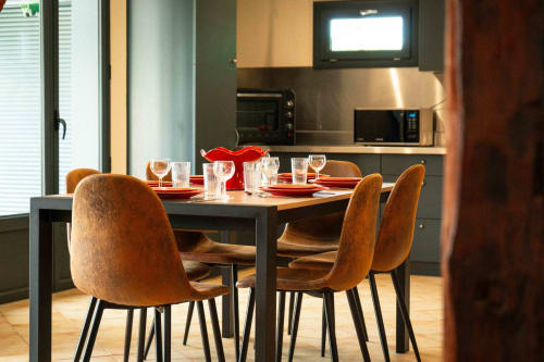 Coin repas moderne du gîte Accolade avec chaises en bois, table noire et cuisine à Châteaudun.