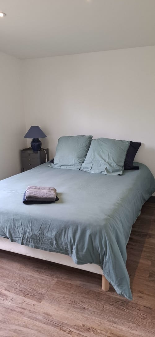 Chambre minimaliste du gîte Accolade à Châteaudun avec literie bleu clair, oreillers, lampe de chevet et parquet