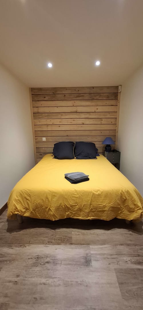 Lit jaune vif aux oreillers noirs et tête de lit en bois dans la chambre du cottage Accolade, Châteaudun
