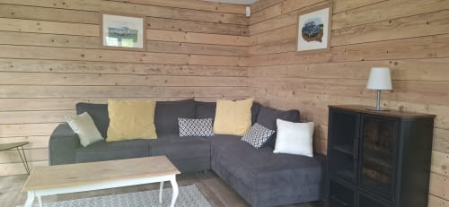 Séjour confortable du gîte de L'étang de la Chartière avec canapé gris, murs en bois, cheminée et vue sur le lac