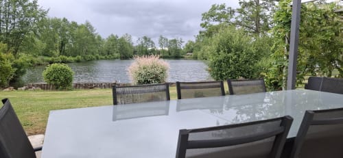 Coin repas en bord de lac au cottage Accolade avec vue sur le plan d'eau, table blanche et chaises noires à Châteaudun
