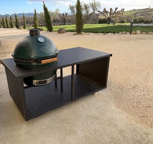 Barbecue en céramique verte intégré à une cuisine d'extérieur noire, avec vue sur les vignobles et cyprès de L'arbre Qui Chante