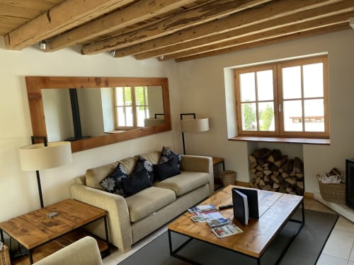 Salon cosy du gîte Le Chalet Savoyard avec poutres en bois, canapé beige, cheminée et vue sur les montagnes