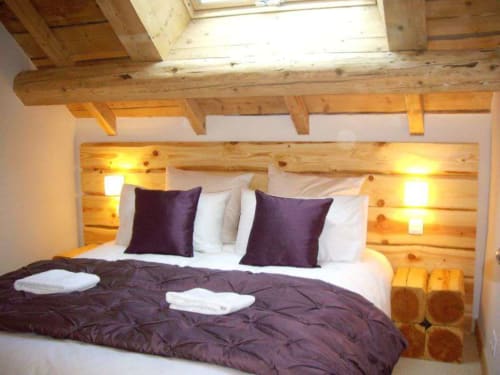 Chambre alpine cosy au Chalet Savoyard, La Plagne avec poutres en bois, linge de lit violet et éclairage chaleureux