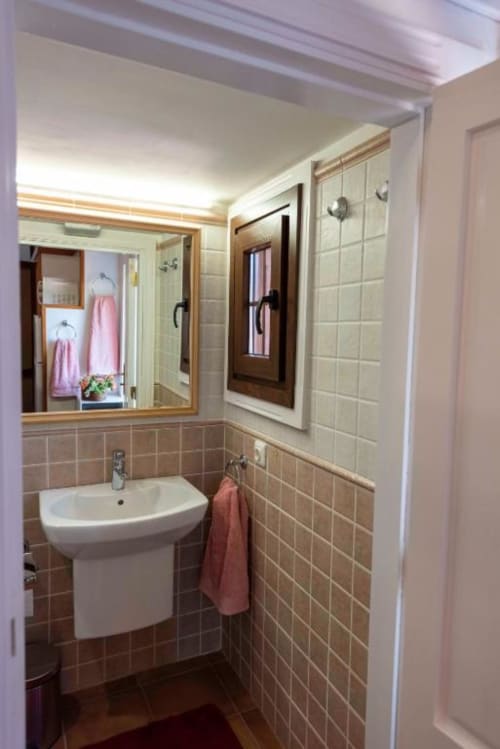 Baño del apartamento Haller Homes en Canarias con lavabo, espejo, baldosas beige y toallas rosas