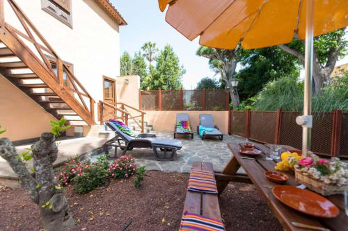 Soleada terraza de Haller Homes en Canarias con tumbonas, comedor, sombrilla amarilla y vistas al exuberante jardín