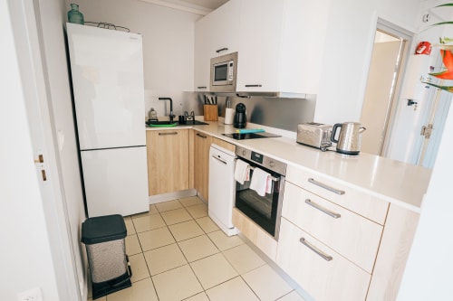 Modern kitchen in La Perle Fleur D'epée apartment, Le Gosier with white appliances, wooden cabinets, and stainless steel