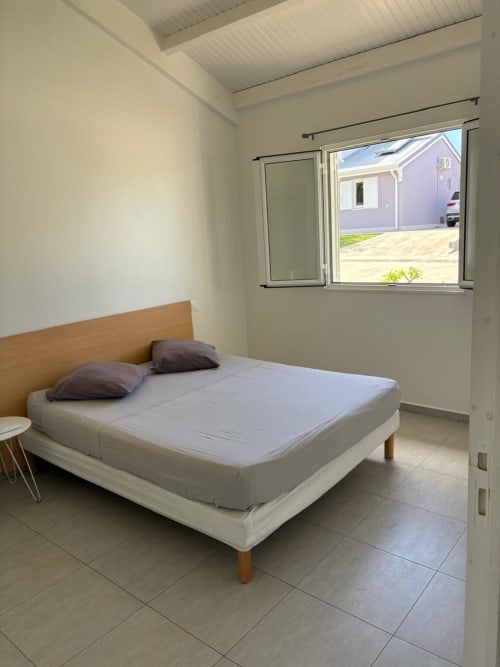 Chambre moderne avec lit queen-size, tête de lit en bois et oreillers gris à la villa Maly Blue Location au Moule, Guadeloupe
