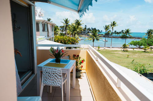 Balcony view at La Perle Fleur D'epée, Le Gosier with sea view, blue awning, dining table, and tropical beach landscape