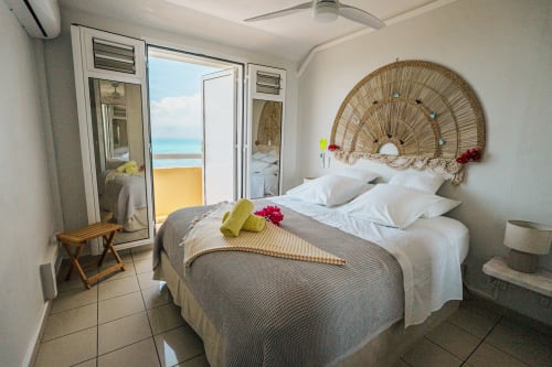 Beachfront bedroom at La Perle Fleur D'epée hotel in Le Gosier with sea view, woven headboard, and balcony access