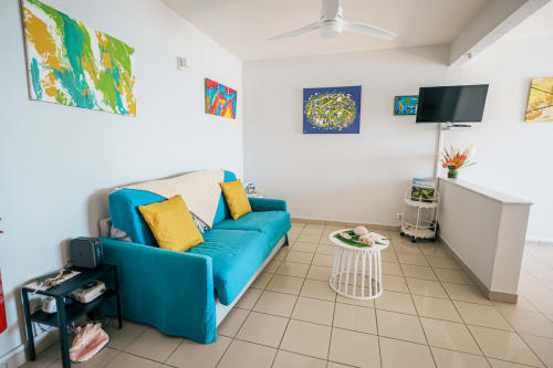 Bright modern living room at La Perle Fleur D'epée hotel with turquoise sofa, colorful artwork, flat-screen TV, and tile
