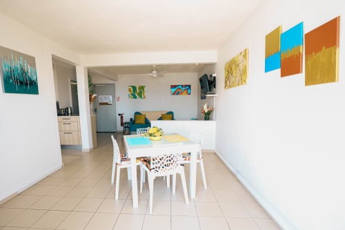 Modern dining and living area in La Perle Fleur D'epée apartment with white furniture, colorful wall art, and sea views in Le