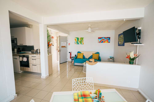 Modern apartment living area at La Perle Fleur D'epée, Le Gosier with open-plan kitchen, blue sofa, colorful artwork and sea