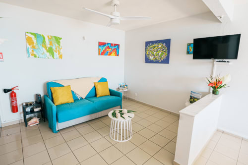 Bright modern apartment living room at La Perle Fleur D'epée in Le Gosier with turquoise sofa, flat-screen TV, and tropical