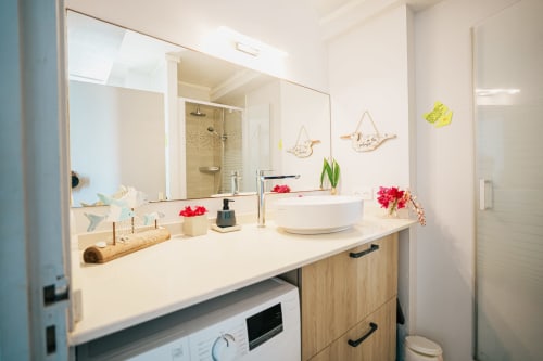 Modern bathroom vanity with round white sink, wooden cabinets, large mirror, and pink flower decor in La Perle Fleur D'Épée