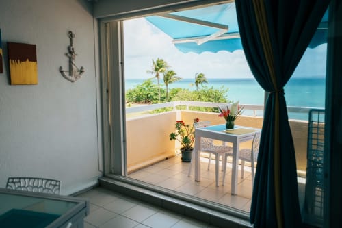 Beachfront apartment balcony at La Perle Fleur D'épée, Le Gosier with ocean view, palm trees, and turquoise sea