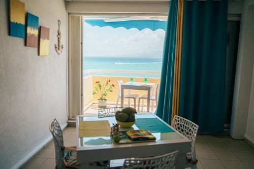 Bright beachfront apartment at La Perle Fleur d'Épée with sea view from balcony, dining area, and turquoise curtains in Le