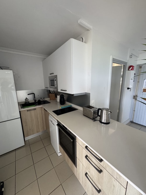 Modern kitchen in La Perle Fleur D'epée apartment, Le Gosier with white cabinetry, stainless steel appliances, and induction
