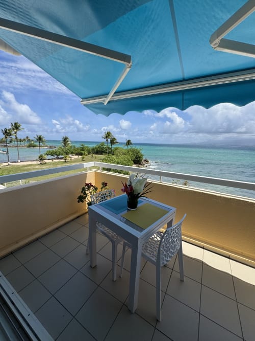 Beachfront balcony at La Perle Fleur d'Épée, Le Gosier with sea view, turquoise awning, and tropical garden.