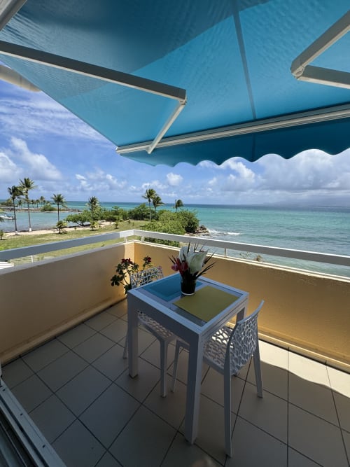 Coastal balcony at La Perle Fleur D'epée hotel in Le Gosier with turquoise sea view, blue awning, and dining setup
