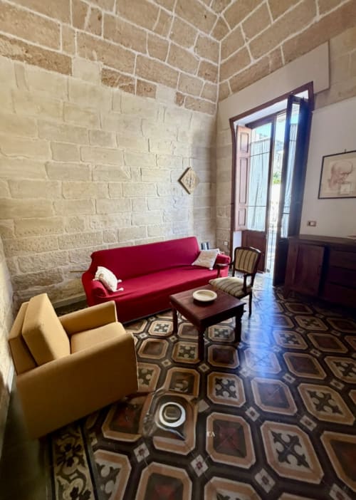 Elegante living room con divano rosso e poltrona gialla, muri in laterizio a vista e pavimenti a piastrelle decorate - HABITARE Lecce