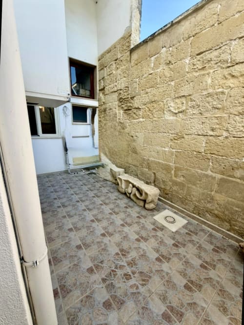 Cortile d'ingresso dell'appartamento HABITARE Astricu a Lecce con pavimento piastrellato, porta moderna bianca e muro in pietra tradizionale