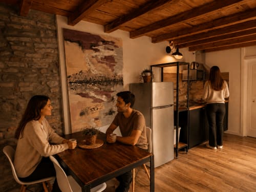 Zwei Gäste genießen Kaffee am Esstisch in einem modernen Loft in Bergamo mit Backsteinmauern, Holzbalken und Edelstahl