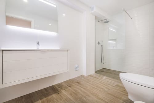 Banheiro moderno no BlueHorizon by SignatureStays em Albufeira com bancada branca, chuveiro walk-in e piso com padrão madeirado