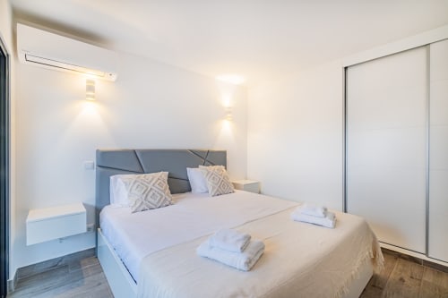 Quarto moderno no BlueHorizon by SignatureStays em Albufeira com roupa de cama branca, cabeceira cinzenta e mobiliário elegante
